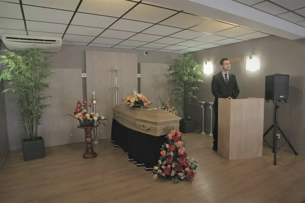 Maître de cérémonie debout près du cercueil dans une salle d'hommage funéraire.