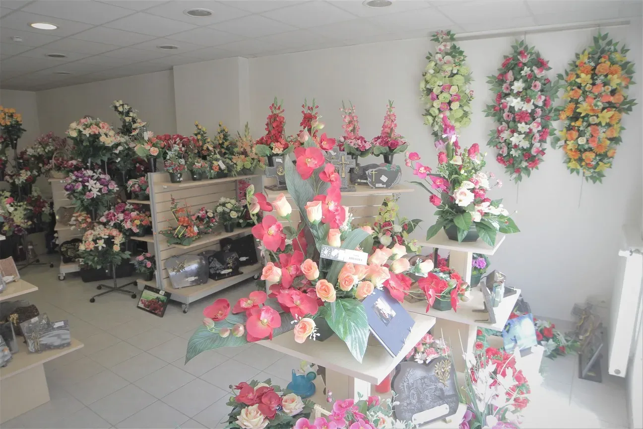 Exposition de fleurs artificielles et couronnes de deuil dans une boutique funéraire.